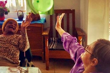 Two elderly women, one white and one Black, toss a green balloon
