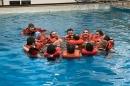 Group of people wearing lifejackets huddle in a circle in a pool